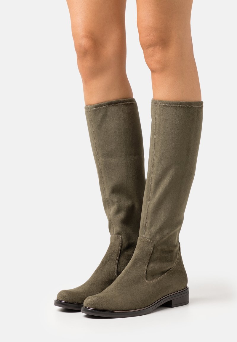 Jambes portant des bottes en daim vert olive montant jusqu'au genou, avec des talons bas et des bouts arrondis sur fond blanc.