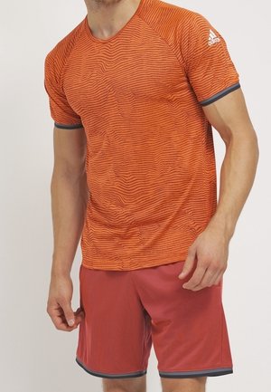 Homme portant un t-shirt orange texturé Adidas à manches courtes et un short de sport orange assorti avec une bordure grise.