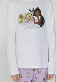 Bílá košile s dlouhým rukávem s grafikou dvou kreslených postaviček a psů. V páru s lehce fialovými pyžamovými kalhotami s hravými potisky psů.