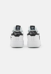 Hvide sneakers med sorte accenter, der har et glat læderoverdel, en gummisål og et signaturlogo på hælen.