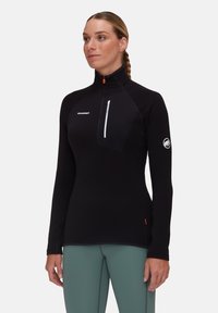 Maglia nera a maniche lunghe con colletto alto, zip a metà, tasca sul petto e logo. Presenta un tessuto texturizzato e dettagli con cuciture a contrasto.