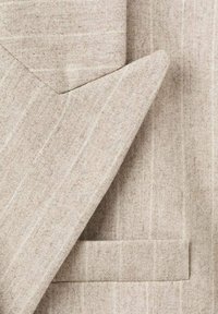 Traje de lino beige con sutiles rayas verticales. Presenta solapas con muesca y un bolsillo en el pecho. Tejido texturizado con un acabado natural.