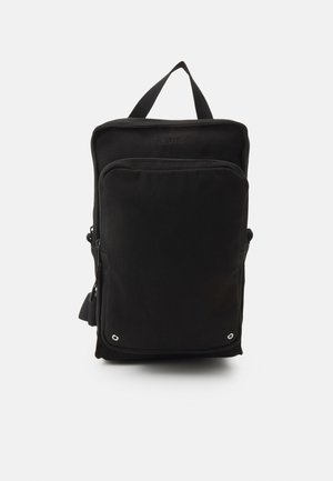 Rucsac din țesătură neagră, cu formă rectangulară, mânere superioare, buzunar frontal cu fermoar și orificii argintii în partea de jos. Design simplu.