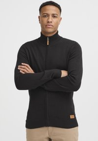 Sort zip-sweater lavet af et glat stof. Har en høj krave, ribbede manchetter og kant, samt et lille mærket lædertag nær taljen.