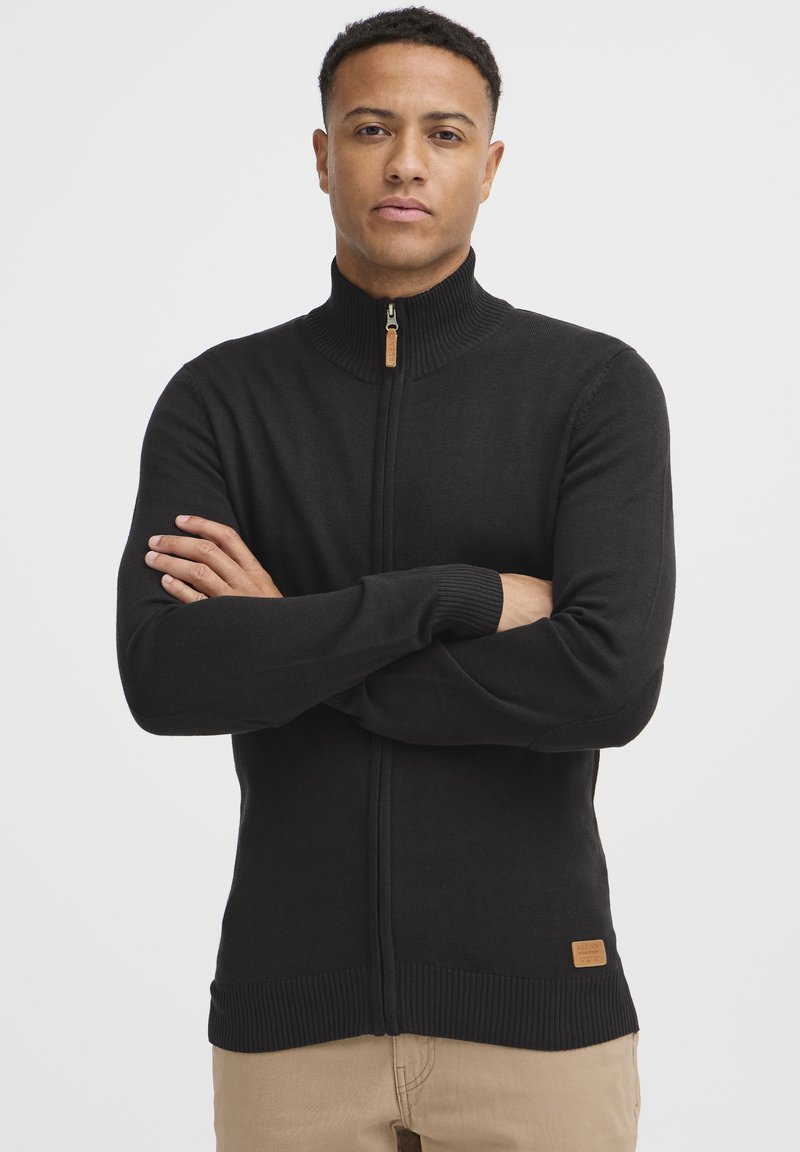 Sort zip-sweater lavet af et glat stof. Har en høj krave, ribbede manchetter og kant, samt et lille mærket lædertag nær taljen.
