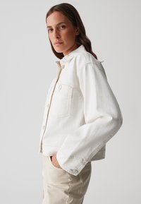 Giacca in denim bianco con colletto a punta, tasche frontali e chiusura a bottoni. Il tessuto ha una superficie liscia e un design accorciato.