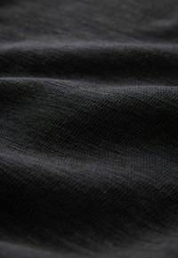 Fekete, texturált anyag közeli képe, amely finom kötött mintázatot és finom redőket mutat, fény- és árnyjátékot kialakítva.