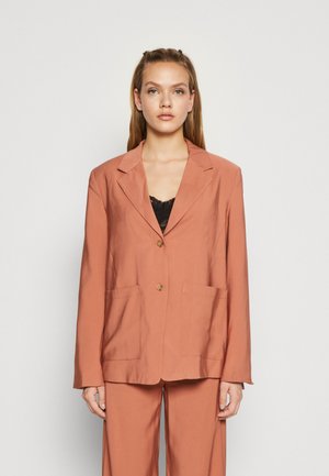 Μπλέιζερ σε ρουστίχ απόχρωση με κοφτές πέτες, δύο μπροστινές τσέπες και κλείσιμο με ένα κουμπί. Λείο ύφασμα με δομημένη σιλουέτα.