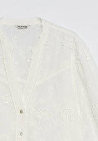 White semi-sheer blouse with floral embroidery, v-neckline, and buttons, labeled "Salsa Jeans" at the collar.