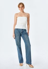 Top blanco sin mangas con un busto ajustado, combinado con jeans de tiro alto azul claro y sandalias de tacón amarillo. Textura suave, diseño casual.