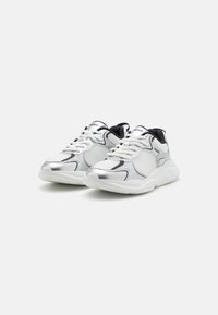 Zapatillas de malla blancas y plateadas con acentos negros, con punta redondeada, diseño con cordones y suela de goma gruesa con agarres texturizados.
