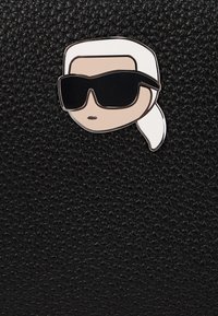El fondo de material texturizado negro presenta un pin de un personaje con cabello blanco, gafas de sol oscuras y una cara beige.