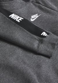 Šedá mikina vyrobená z měkké látky, s černým pruhem a textem "NIKE" a bílým logem na hrudi a rukávu.