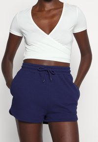 Haut portefeuille blanc à manches courtes avec un décolleté en V, associé à un short bleu foncé à taille élastique, doté de poches latérales et d'un cordon de serrage.