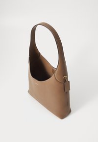 Sac à bandoulière en cuir marron avec une large sangle, ouverture en haut, logo discret de la marque et étiquette rectangulaire attachée avec une chaîne dorée.