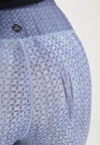 Legginsy z wysokim stanem w jasnoniebieskim kolorze, z teksturowanym wzorem liści, subtelnym połyskiem i kontrastowym przeszyciem wzdłuż boków.