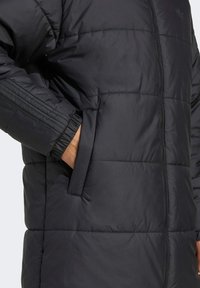 Juodas pūkinis švarkas su užtrauktuku priekyje, šoniniais kišeniais, siūtu raštu ir elastingomis rankovėmis, teikiantis šilumą ir komfortą elegantiškame dizainas.