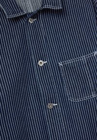 Navy blue striped shirt made of fabric with a button-down collar, featuring a button closure, left chest pocket, and contrasting white stripes.