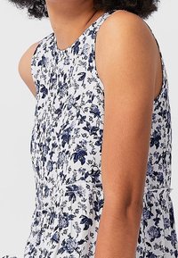Il vestito floreale presenta una base bianca con motivi di fiori blu, design senza maniche e vita arricciata per una silhouette fluida.