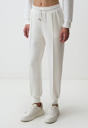 Witte sweatpants met een elastische tailleband, trekkoorddetails, zijzakken en taps toelopende enkels, gecombineerd met witte sneakers.