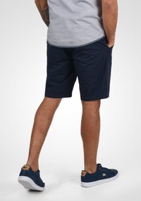 Navy blue shorts made of fabric with a smooth texture, featuring side pockets and a straight-cut design. Paired with dark blue sneakers.