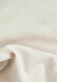 Mjukt, ljust beige stickat tyg med fin ribbad struktur, varsamt vikt för att skapa mjuka kurvor och skuggor.