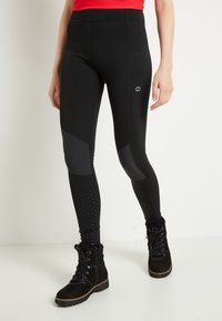 Svarta träningsleggings med paneldesign, texturerade nedre sektioner och logodetalj på låret, kombinerade med svarta snörstövlar.