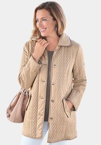 Beige gesteppte Jacke mit hohem Kragen, Knopfverschluss und zwei seitlichen Taschen. Glatte Textur mit Zickzackmuster und kontrastierenden Besätzen.