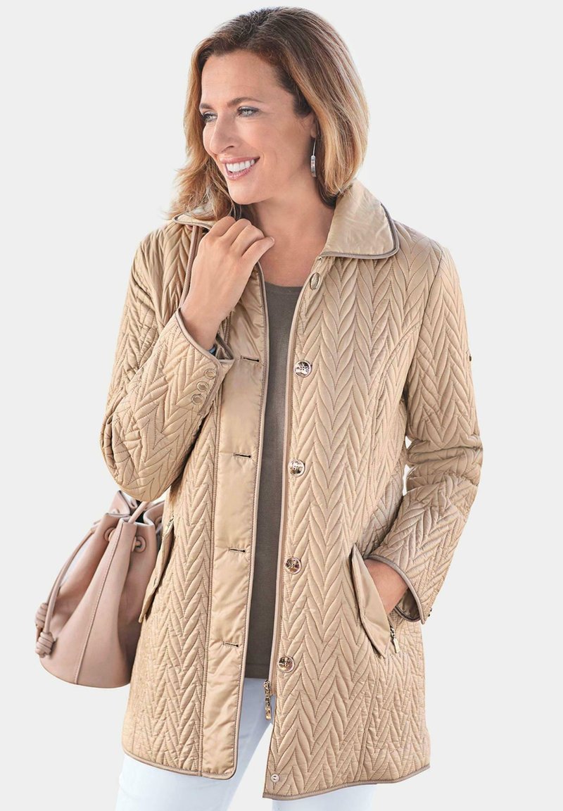 Beige gesteppte Jacke mit hohem Kragen, Knopfverschluss und zwei seitlichen Taschen. Glatte Textur mit Zickzackmuster und kontrastierenden Besätzen.