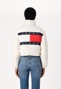 Giacca a vento bianca con colletto alto, caratterizzata da una striscia logo blu, rossa e bianca sul retro. Abbinata a jeans in denim blu.