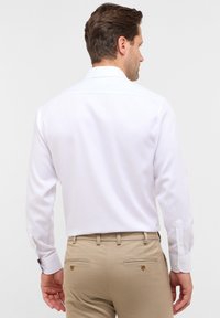 Witte lange mouwen blouse met een eenvoudige ontwerp, met knoopmanchetten en een klassieke kraag, gecombineerd met beige broeken met zijzakken.