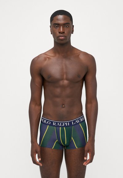 Boxershorts mit einem dunkelgrünen und navyblauen Streifenmuster, das gelbe Linien und einen elastischen, navyblauen, gebrandeten Bund aufweist.