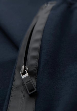 Námořnická látka s černým zipem, na kterém je uvedeno jméno značky "OMBRE". Hladký povrch a elegantní design se zipem ve tvaru obdélníku.