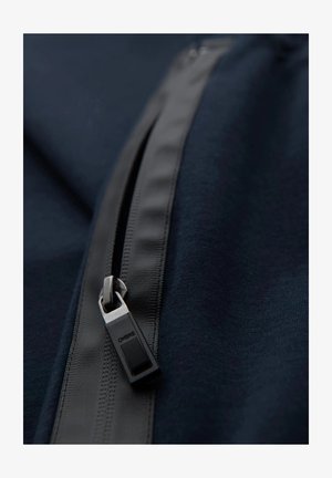 Granatowy materiał z czarnym zamkiem błyskawicznym z nazwą marki "OMBRE." Gładka tekstura i elegancki design z uchwytem zamka w kształcie prostokąta.