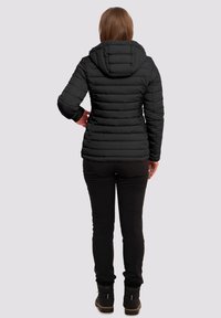 Chaqueta de plumas negra con capucha, con un diseño acolchado. Combinada con pantalones negros y botas negras. Textura suave y silueta ajustada.