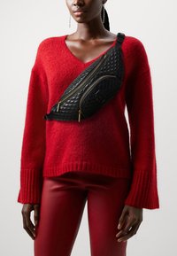 Mustekattu musta nahkainen olkapussukka kultaisilla vetoketjuaksenteilla, yhdistettynä punaiseen neulepaitaan ja punaisiin tiukkoihin housuihin.