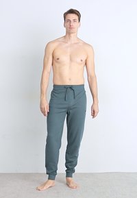 Grüne Jogginghosen aus Stretch mit einem elastischen Bund und Kordelzug, ausgestattet mit einem schmal zulaufenden Beindesign. Glattes Material ohne sichtbare Muster.