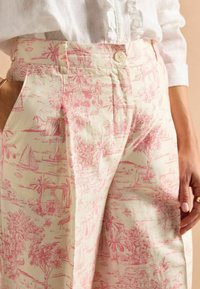 Svetlo krémové nohavice s ružovým vzorom toile, ktorý obsahuje scenické prvky ako palmy a plachetnice. Vyrobené z textúrovaného materiálu.