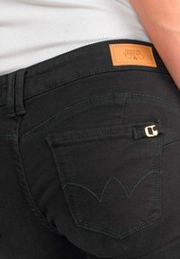 Jeans en denim noir au design ajusté, dotés d'une patch en cuir marron à la taille et d'un motif de couture verte sur la poche arrière.