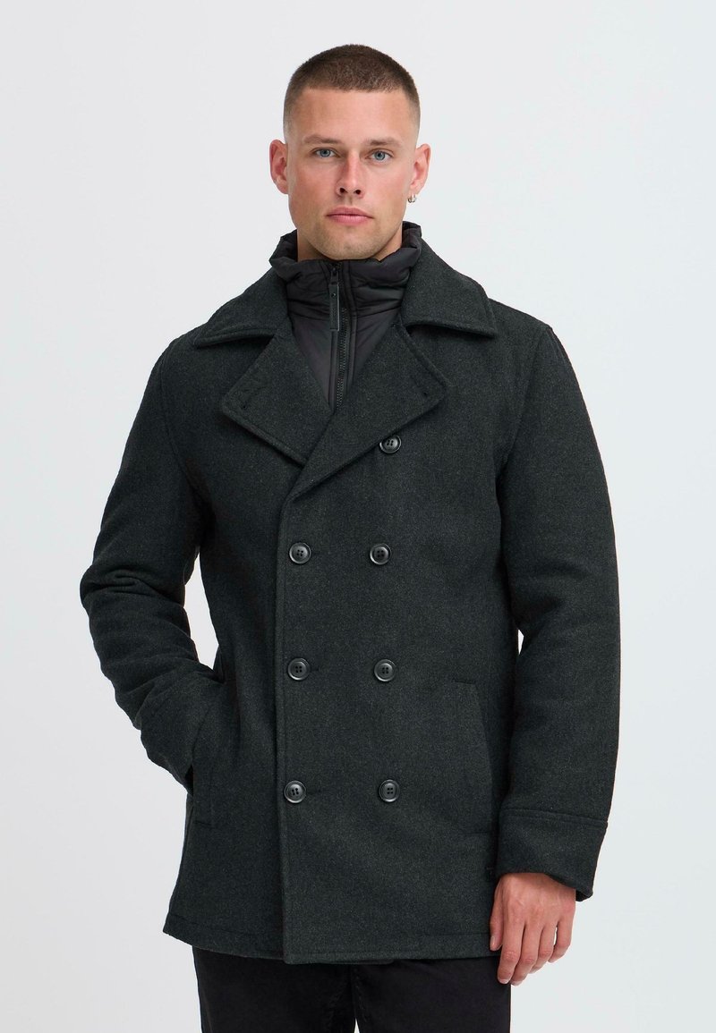 Mørkegrå uld peacoat med dobbeltbrystet design, store knapper og sidelommer, lagd over en sort lynlås-puffer.