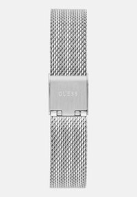 Srebrny metalowy pasek do zegarka z siateczki z prostokątnym zapięciem z wygrawerowanym logo "GUESS", o gładkiej fakturze i eleganckim designie.