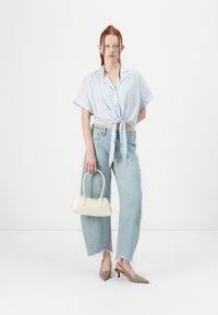 Camisa amarrada de mangas curtas às riscas azul claro, jeans largas desbotadas com barras desfiadas, mala mini bege e sapatos de salto com bico fino.