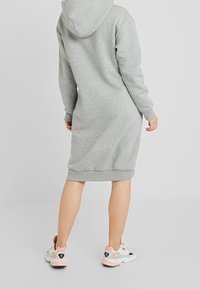 Vestido de sudadera con capucha gris, de mangas largas y dobladillo acanalado, combinado con zapatillas blancas y en tonos pastel con detalles en negro.