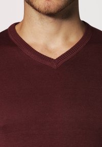 Bordeauxrode V-hals trui gemaakt van gestructureerde gebreide stof, met een geribbelde kraag en een glad, aansluitend ontwerp.