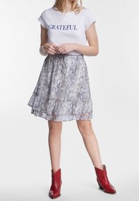 Camiseta blanca de manga corta con el texto "GRATEFUL", combinada con una falda gris fluida y estampada, y botas rojas hasta el tobillo.