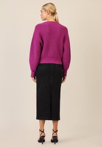 Gehaakte magenta trui met verlaagde schouders, gecombineerd met een zwarte midi-rok met kleine zilveren details en een zijsplit, gedragen met zwarte hakken.