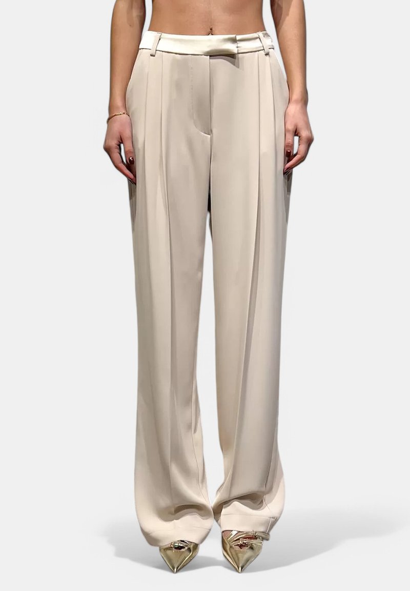 Pantaloni beige a gamba larga in tessuto morbido, con vita alta, pieghe e abbinati a tacchi metallici a punta.