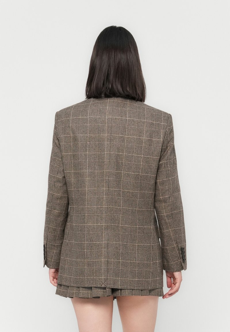 Blazer a quadri marrone con una vestibilità strutturata, spacchetto sul retro e polsini abbottonati. Realizzato in un tessuto testurizzato con linee e motivi a contrasto.
