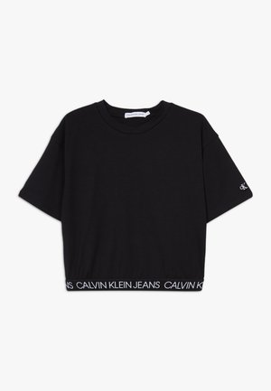 T-shirt noir court à manches courtes, ourlet élastique marqué "Calvin Klein Jeans," et petit logo "CK" sur la manche gauche.