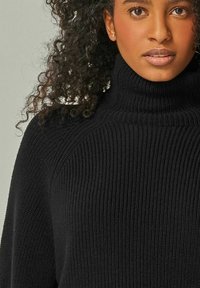 Schwarzer gestrickter Rollkragenpullover mit geripptem Textur, hoher Kragen und lockerer Passform. Weiches Material ohne sichtbare Muster oder Akzente.